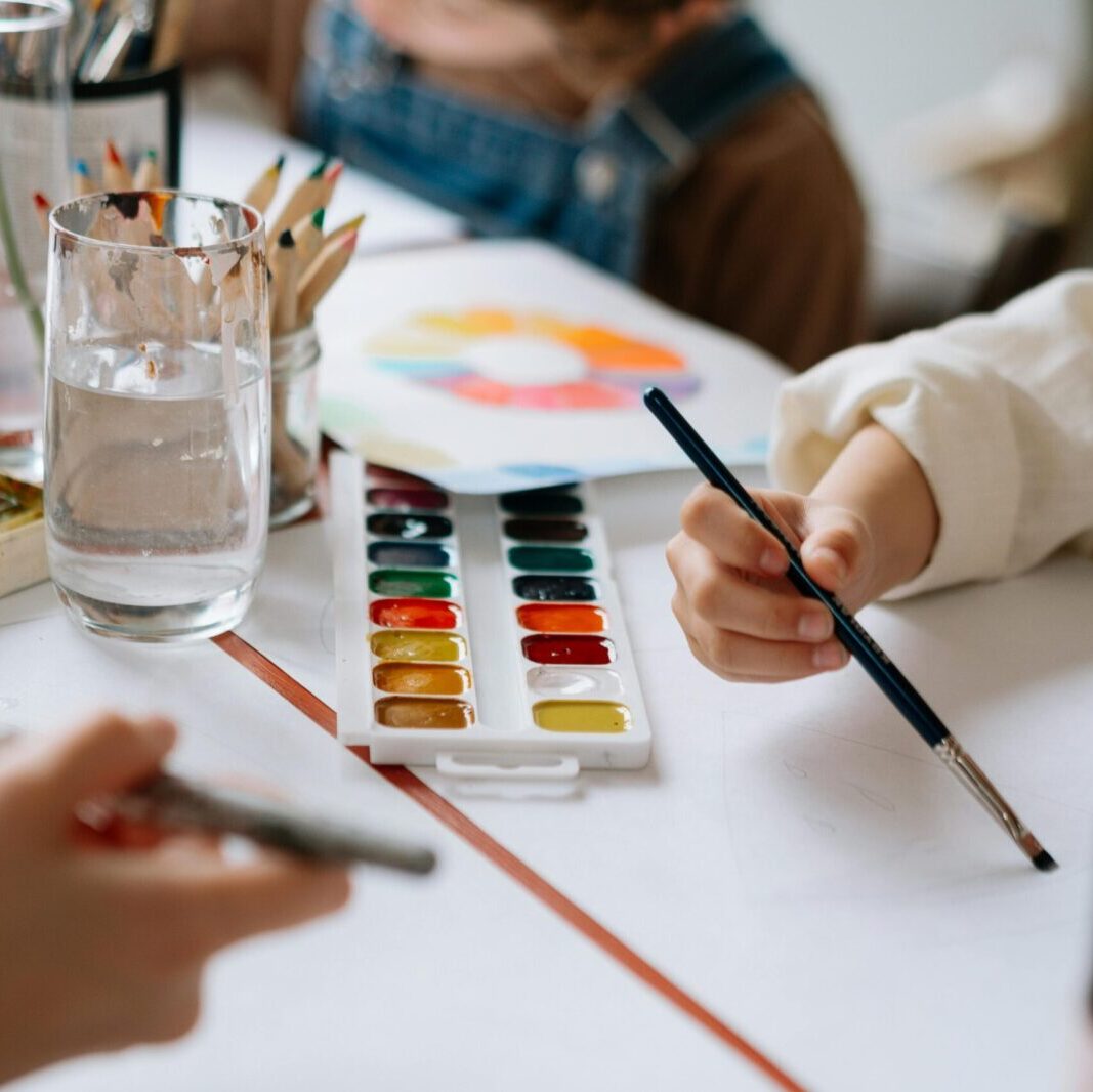 Children's hands holding paintbrushes while painting with watercolors during a creative art session.